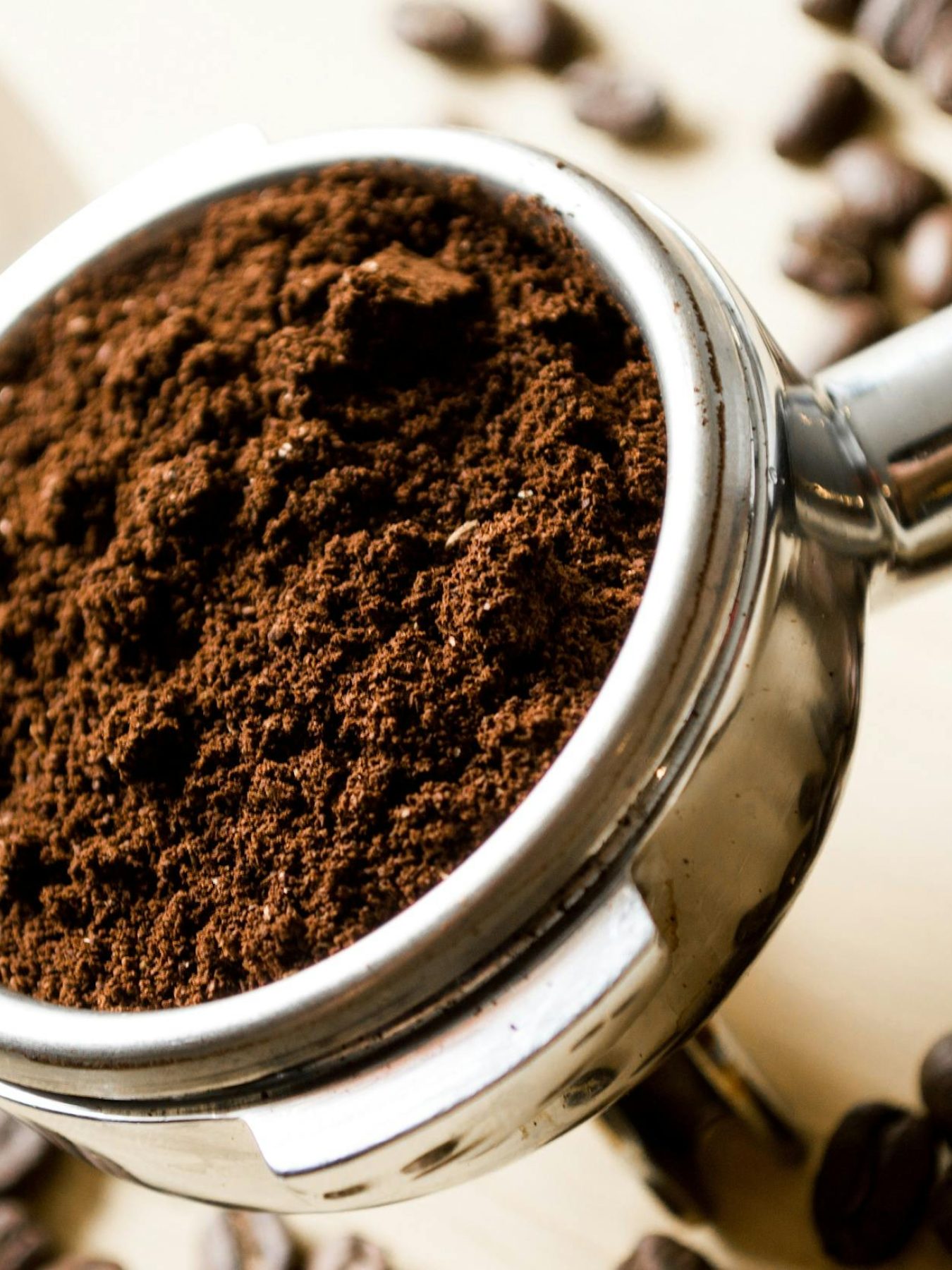 Close-up of freshly ground coffee in a portafilter with scattered coffee beans.